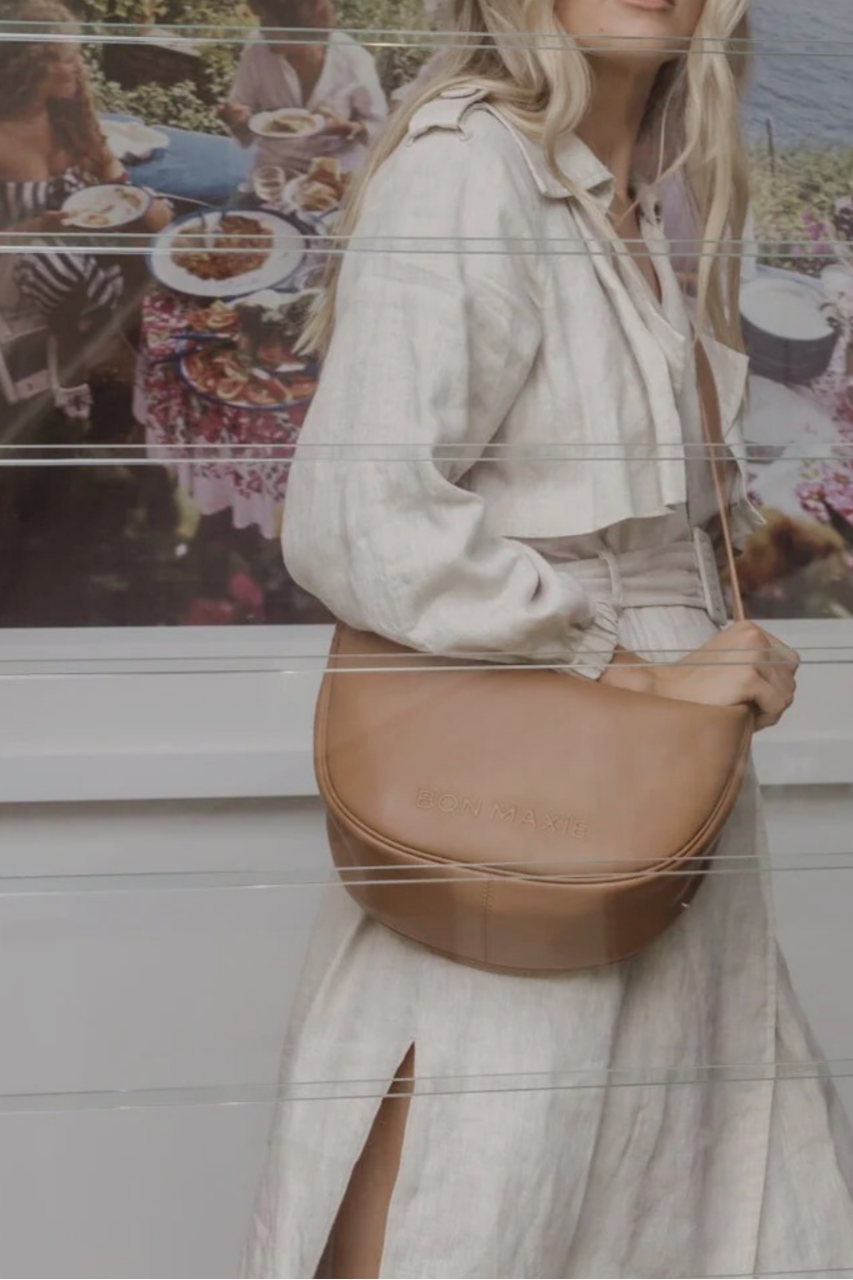 Woman holding a brown leather bag with a blurred outdoor scene in the background