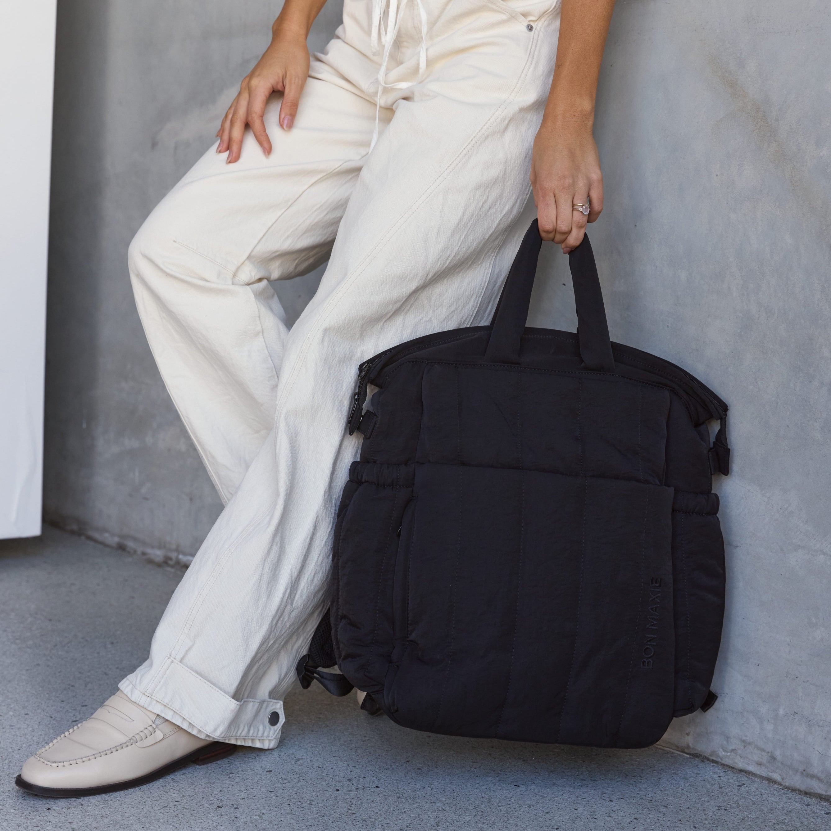 Person holding a black backpack against a neutral background