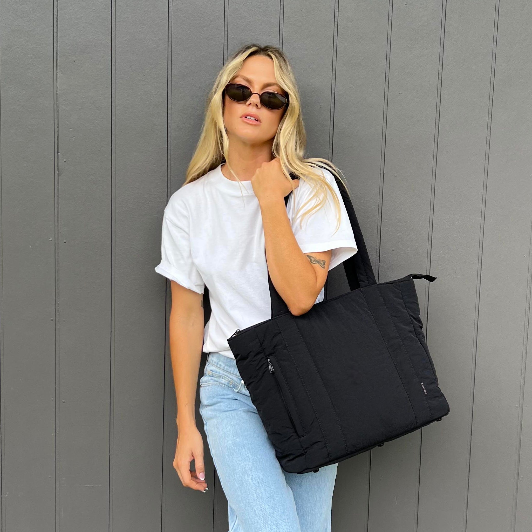 Woman holding a black bag against a gray wall