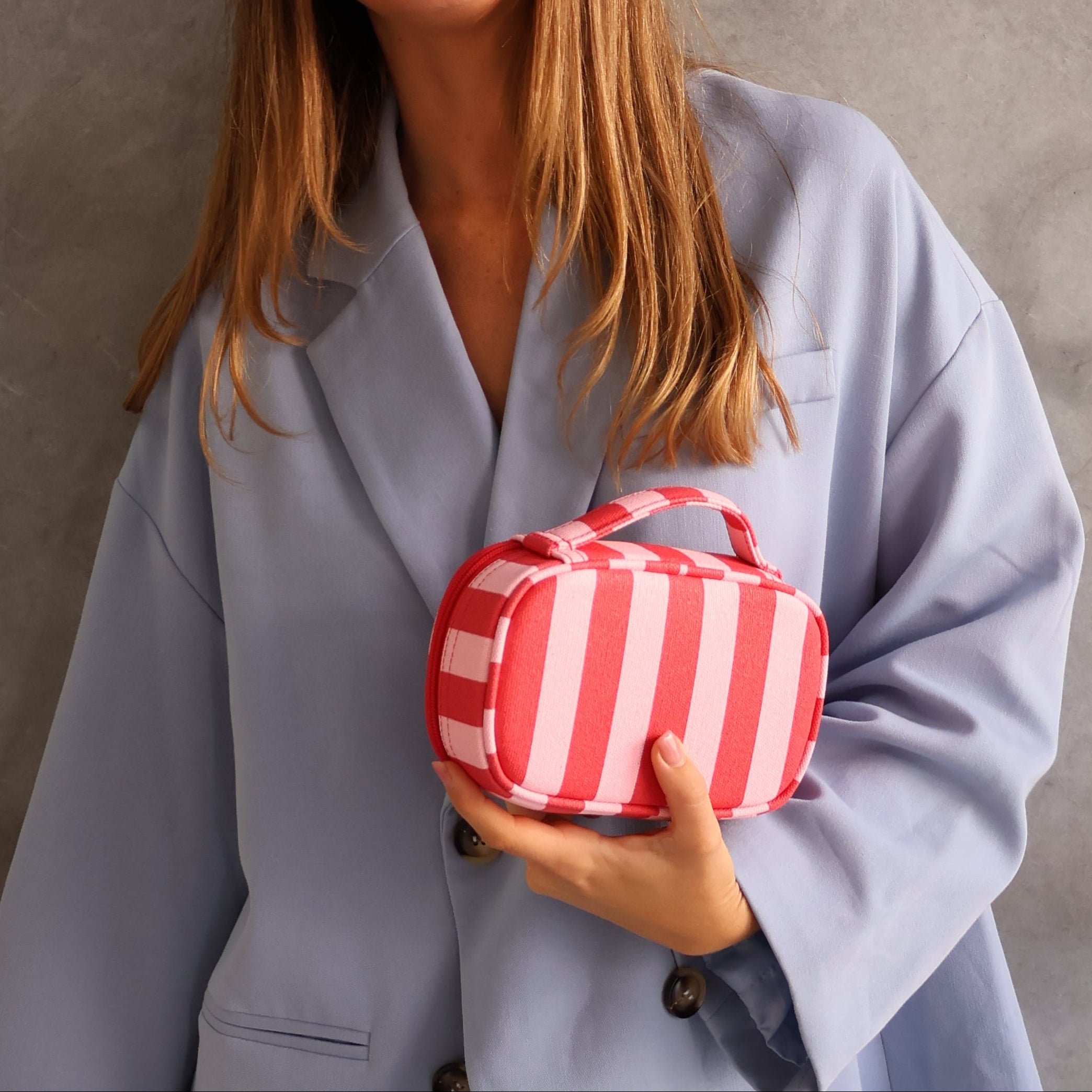 Woman holding a red and white striped bag against a gray background