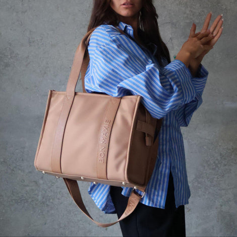 Woman holding a tan tote handbag with a brand logo against a gray background