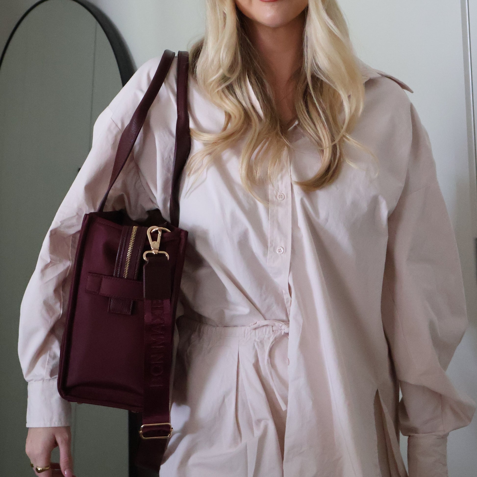 Woman holding a maroon handbag in front of a mirror