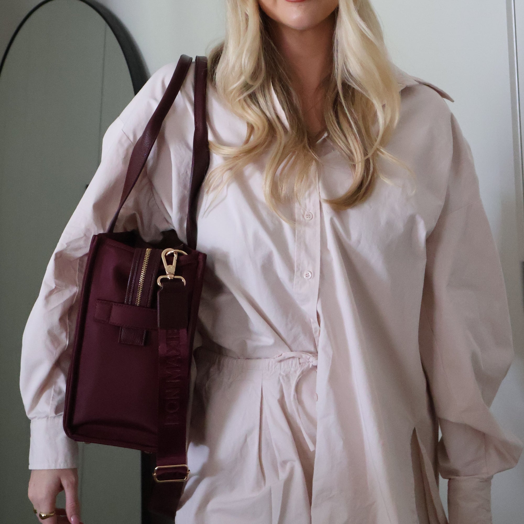 Woman holding a maroon handbag in front of a mirror