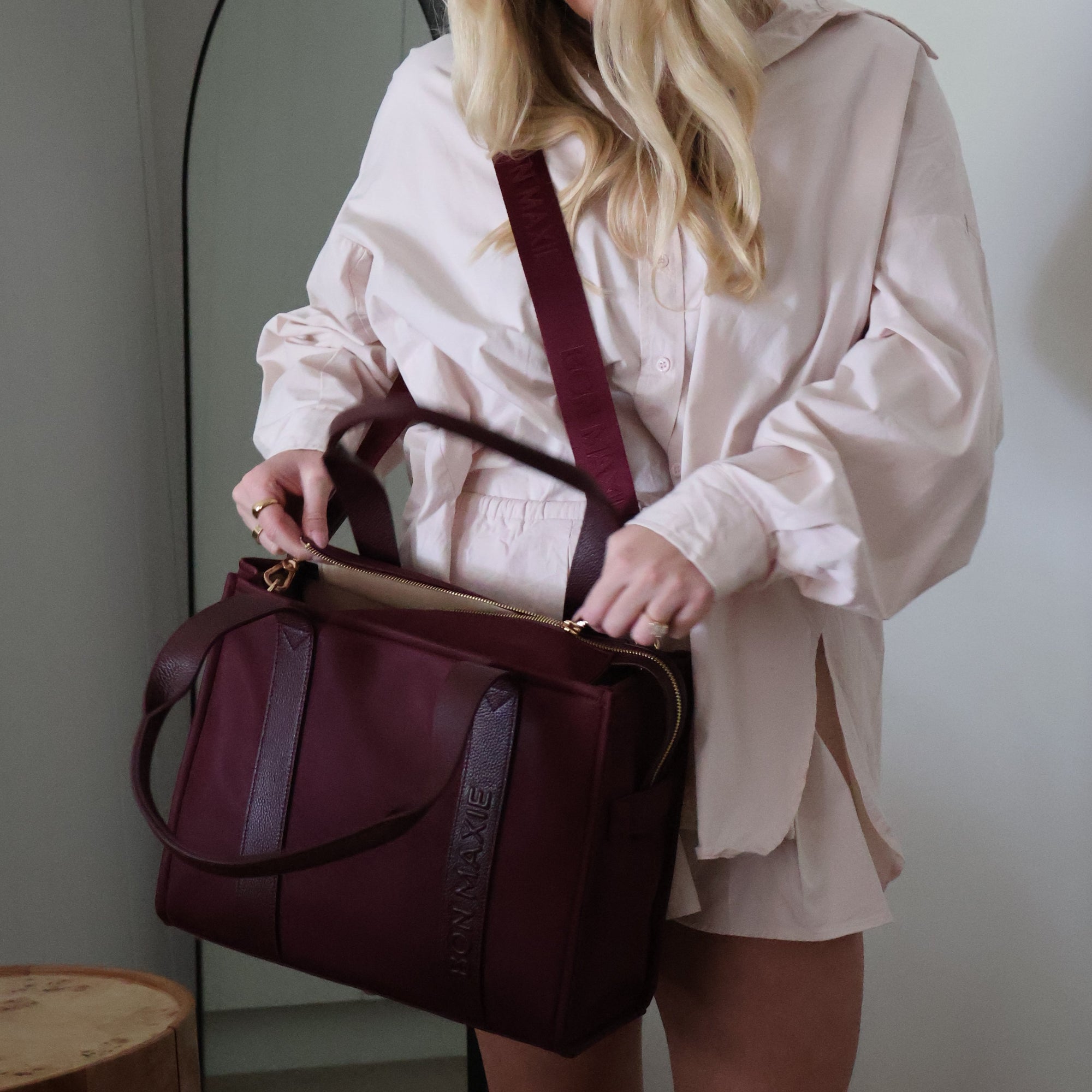 Woman holding a burgundy tote bag with zip open