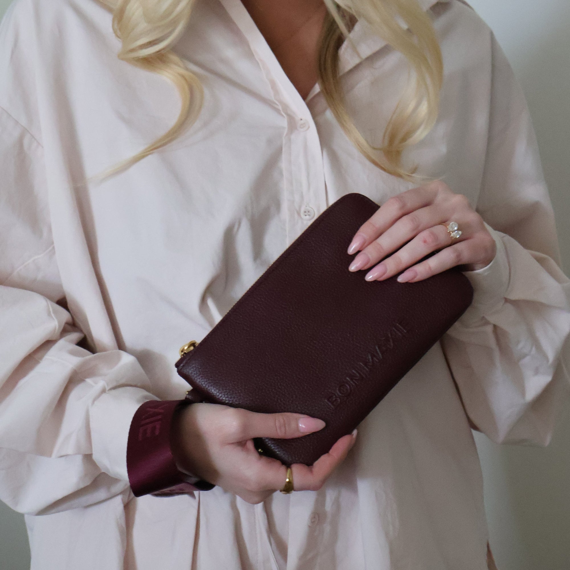 Woman holding a burgundy leather clutch with 'bon maxie' branding against a neutral background