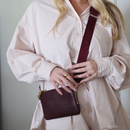 Woman holding a maroon handbag against a neutral background