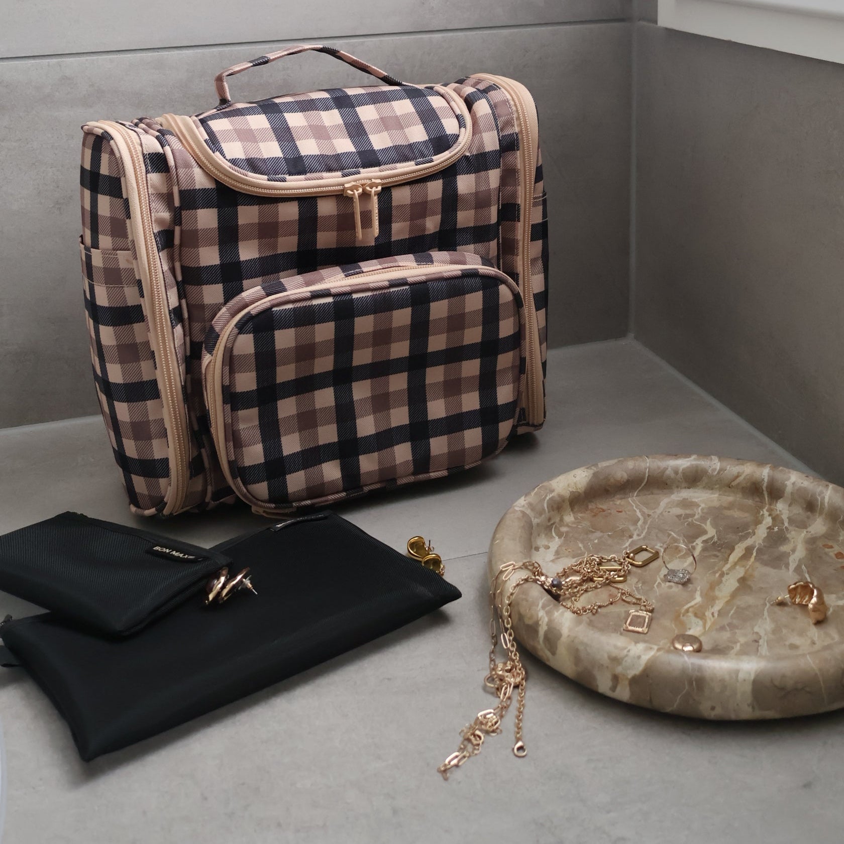 Plaid toiletry bag with black pouches on gray surface.