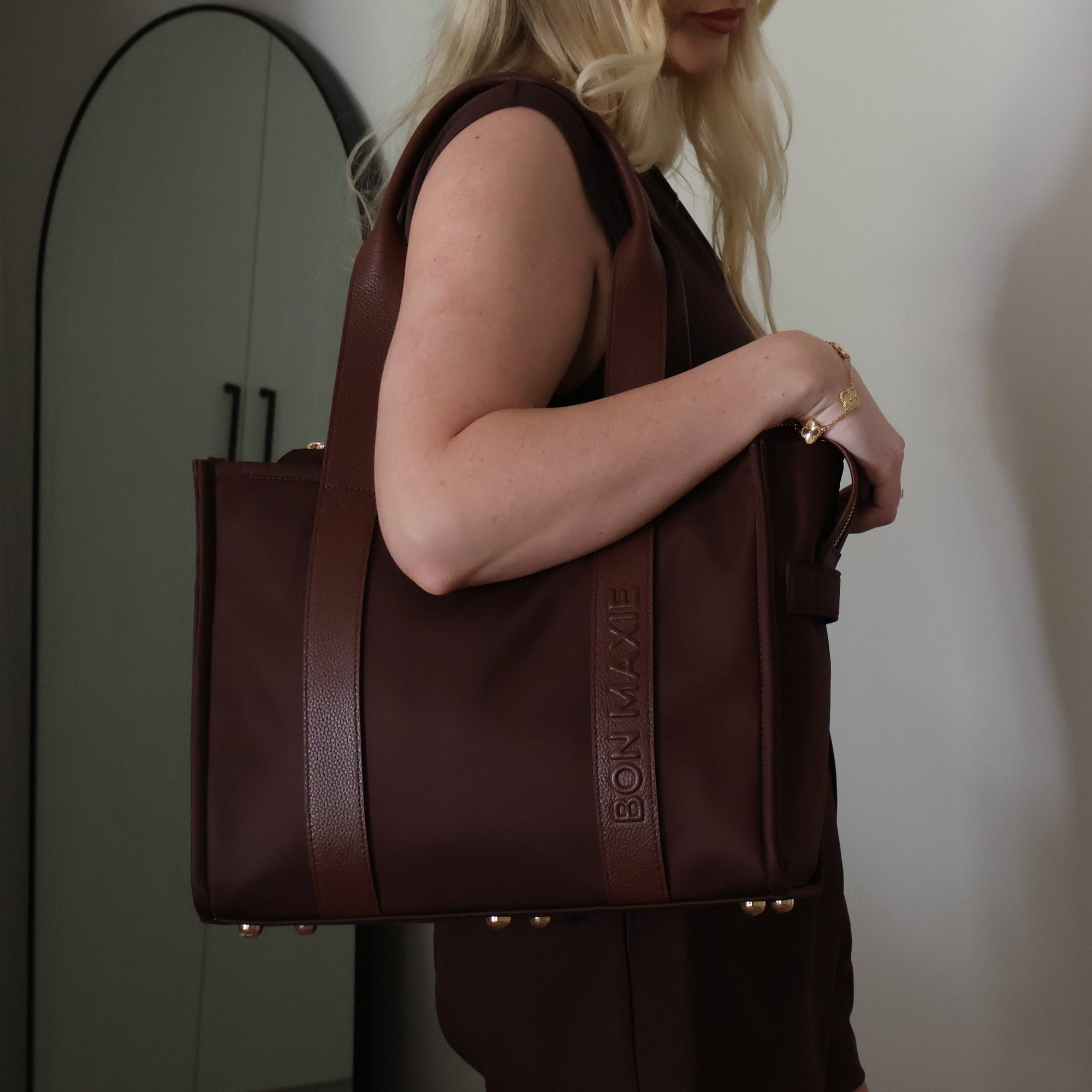 Woman holding a brown nylon and leather tote bag against a plain background