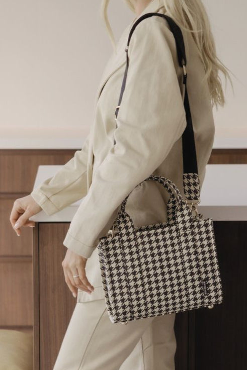 Woman holding a houndstooth patterned handbag in an indoor setting