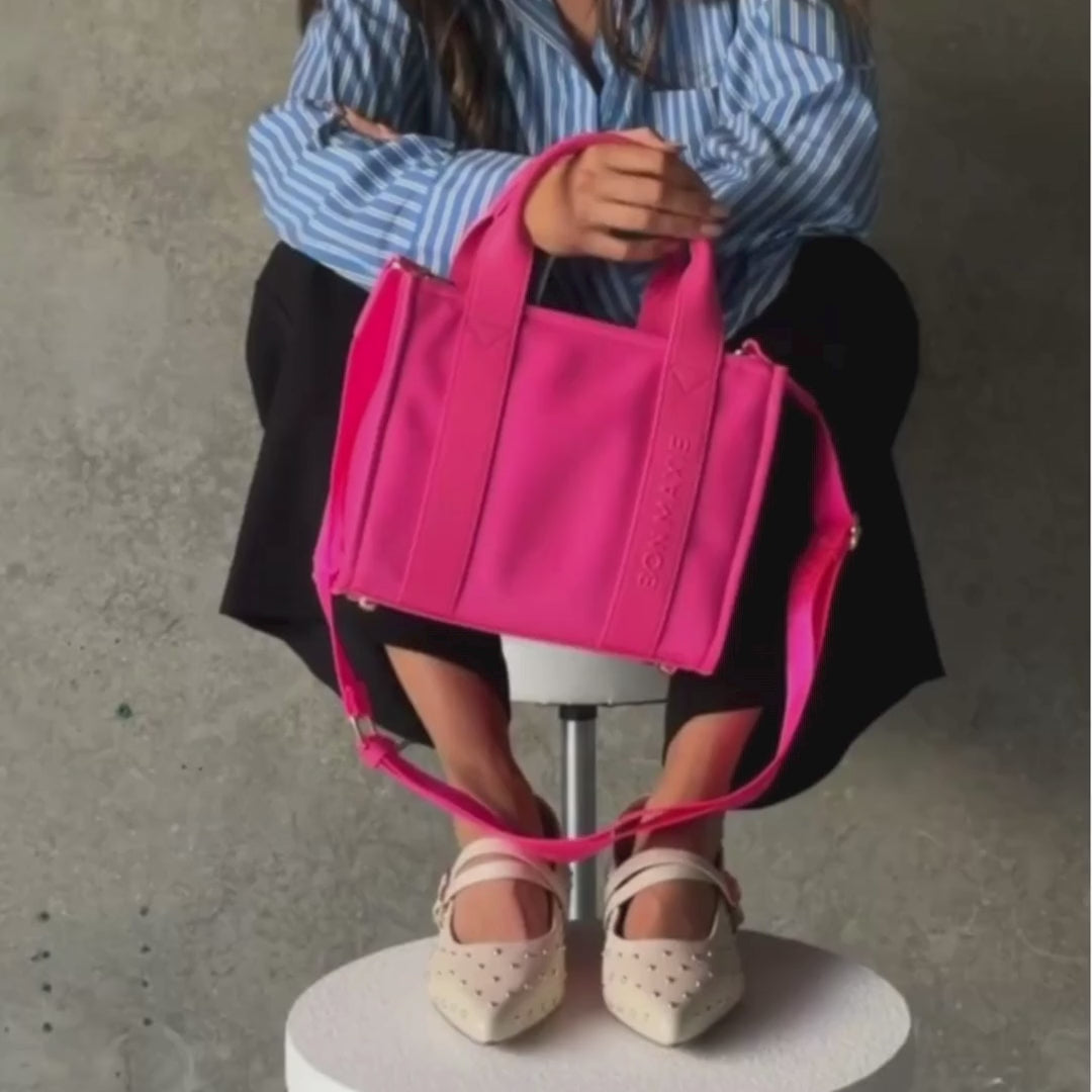 Load video: Woman demonstrating mini nylon leather tote in neon pink