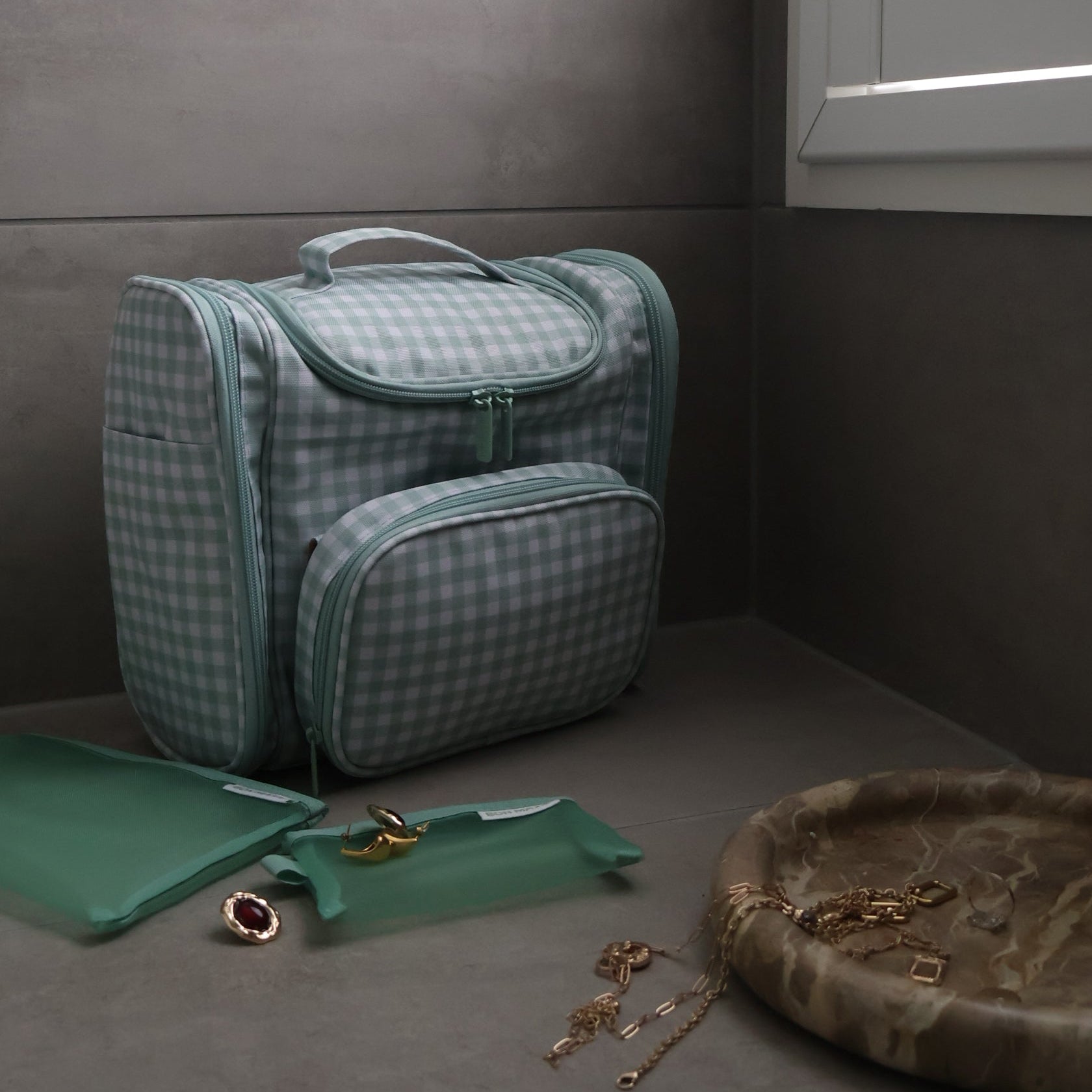 Green checkered bag hanging on a hook against a gray wall with a window in the background.