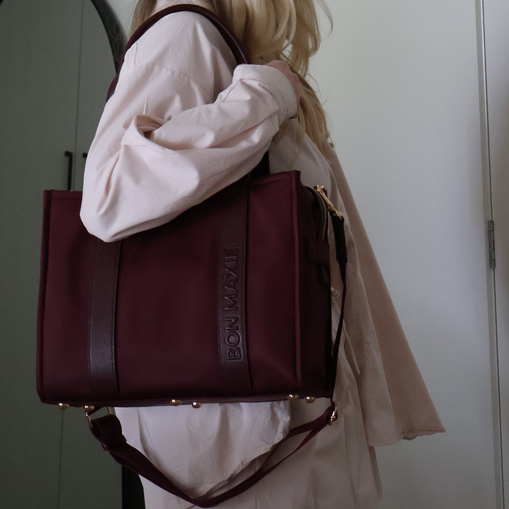 Person holding a maroon tote bag with 'bon maxie' branding on a white background.