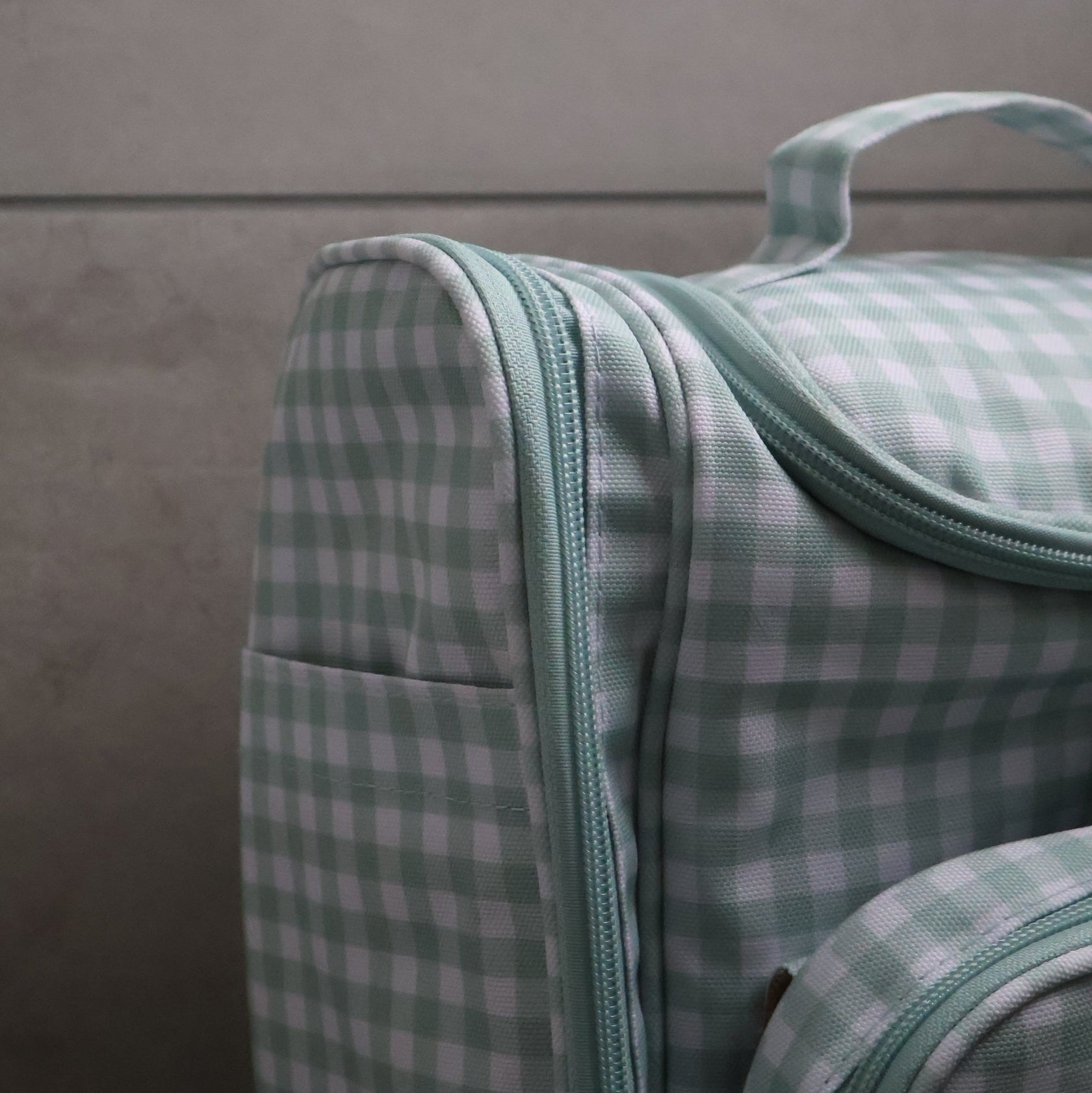 Green and white checkered toiletry bag with a zipper on a gray background